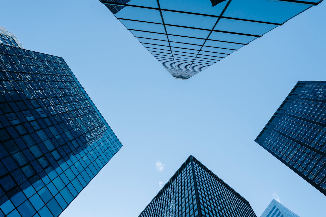 Low angle view of modern skyscrapers with glass facades against a bright blue sky.